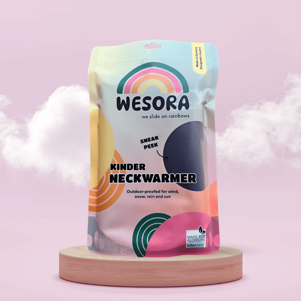 Fleece Neckwarmer -Midnight Blue Kid in einer bunten, wiederverwendbaren Verpackung mit Regenbogen-Logo und Recycling-Hinweis, auf Holzsockel vor rosa Hintergrund.