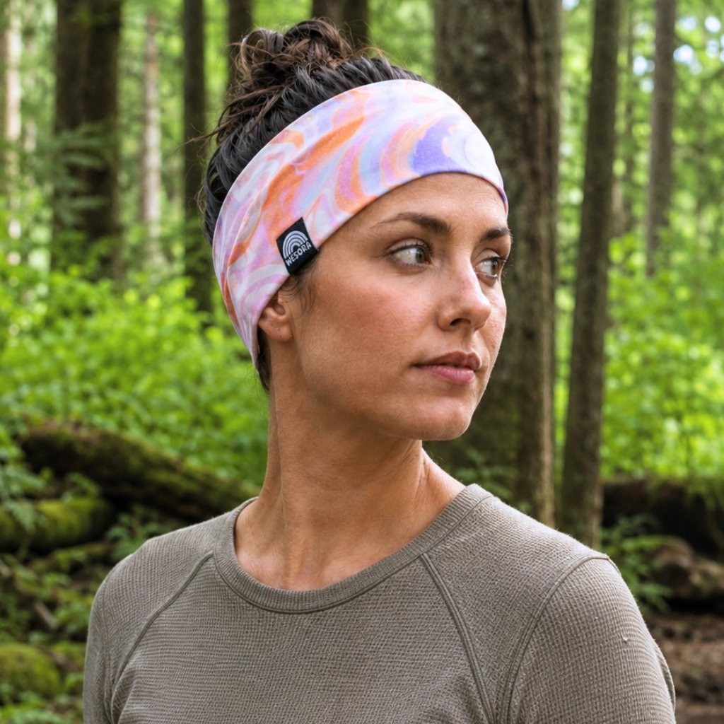 Stirnband - Melting Sunrise mit verquirlten Rottönen, getragen von Frau im Wald, zeigt handgenähte Qualität und elastischen Komfort.