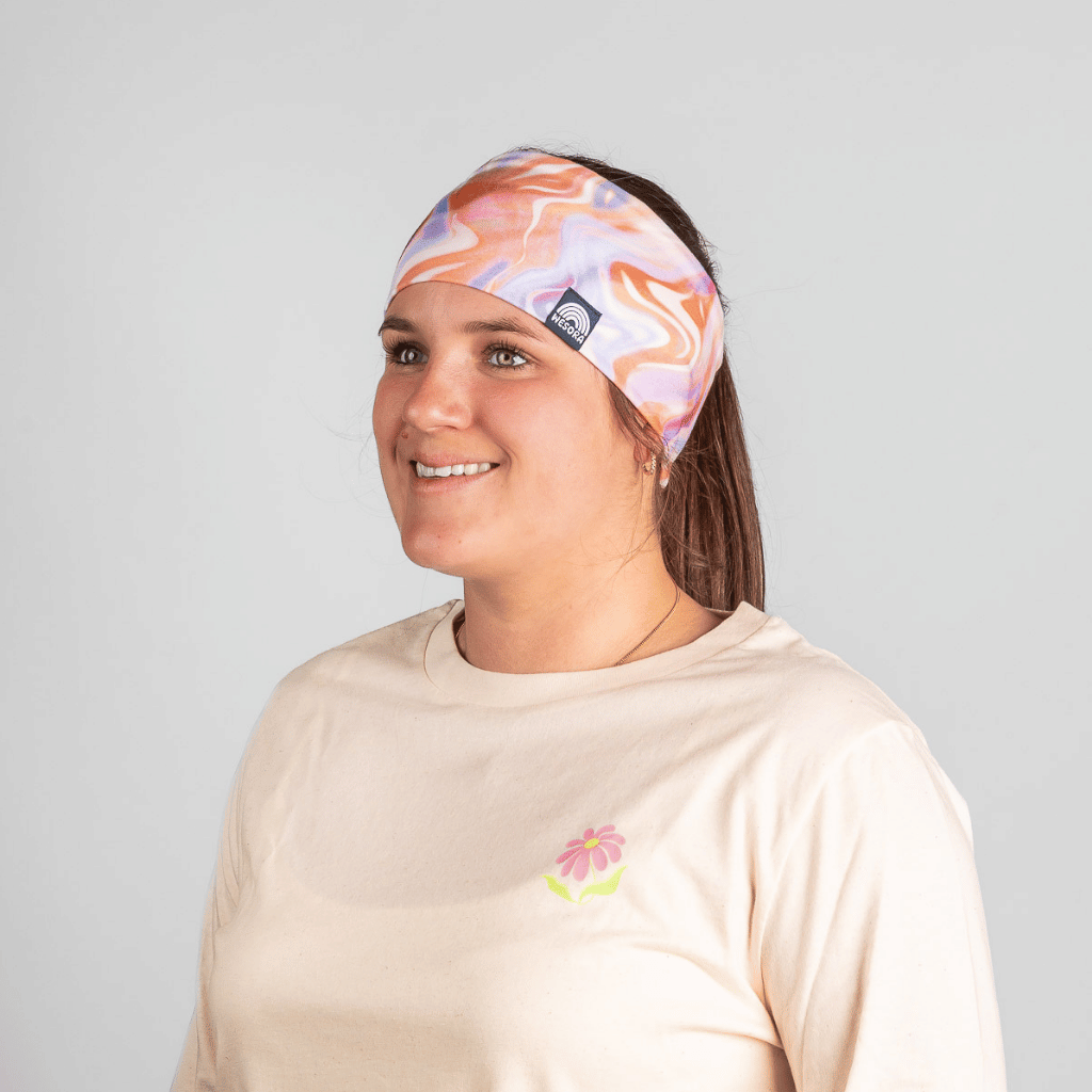 Stirnband - Melting Sunrise mit pastellfarbenem Wirbelmuster, getragen von einer lächelnden Frau, die nach rechts schaut, vor grauem Hintergrund.