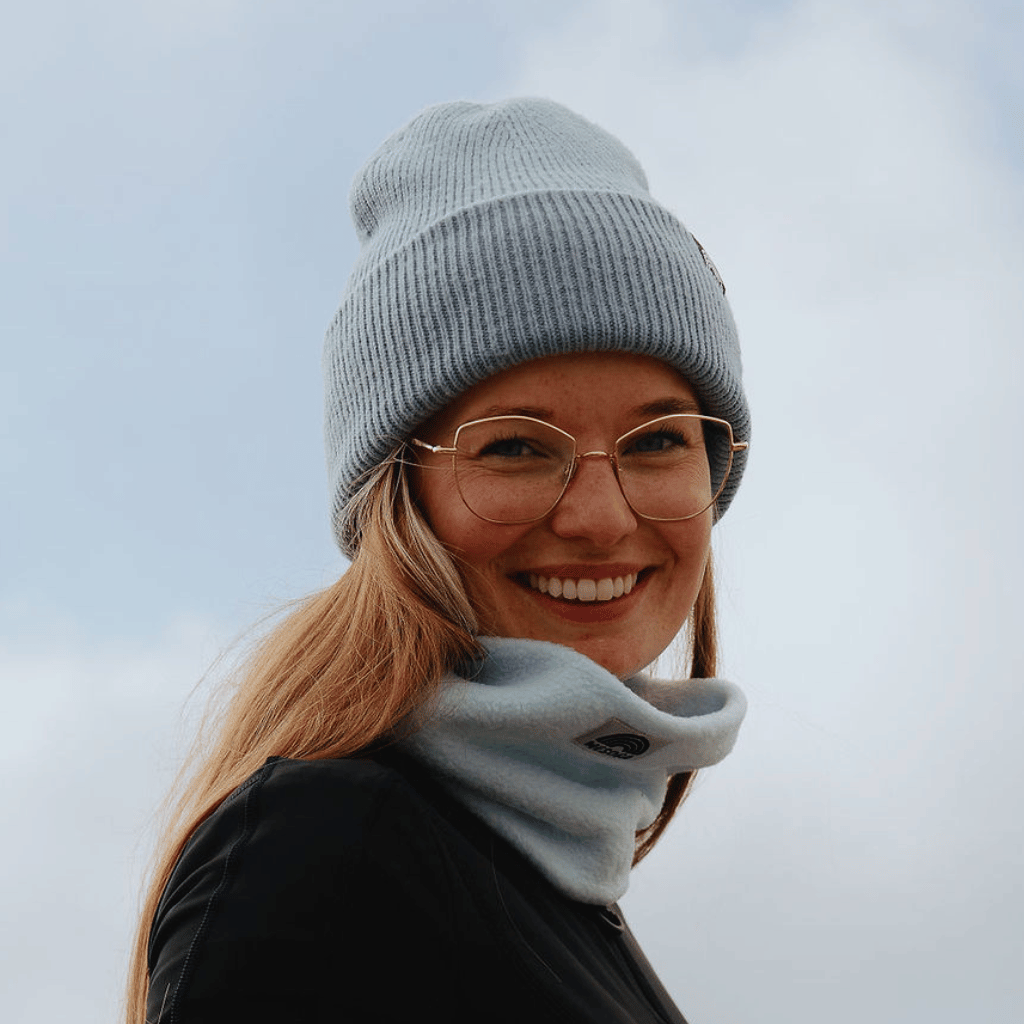 Neckwarmer & Beanie Bundle - Blau, getragen von lächelndem Modell im Freien, Nahaufnahme bei Tageslicht, klare Brille, hellgraue Strickmütze und passender Fleece-Schal.