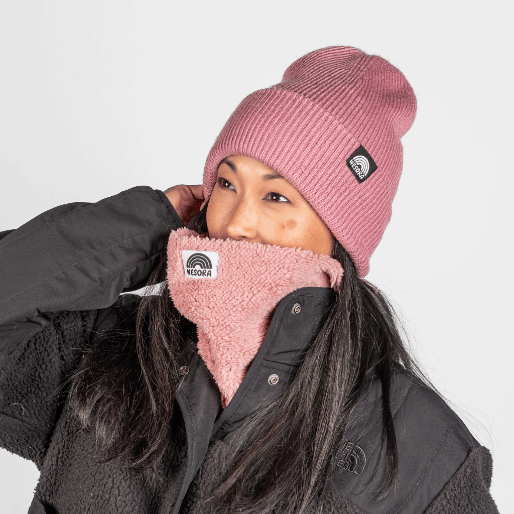 Neckwarmer & Beanie Bundle - Fluffy Rose, getragen von Person in schwarzer Jacke, zeigt Logo-Patches auf beiden Teilen. Ideal für kalte Abenteuer.