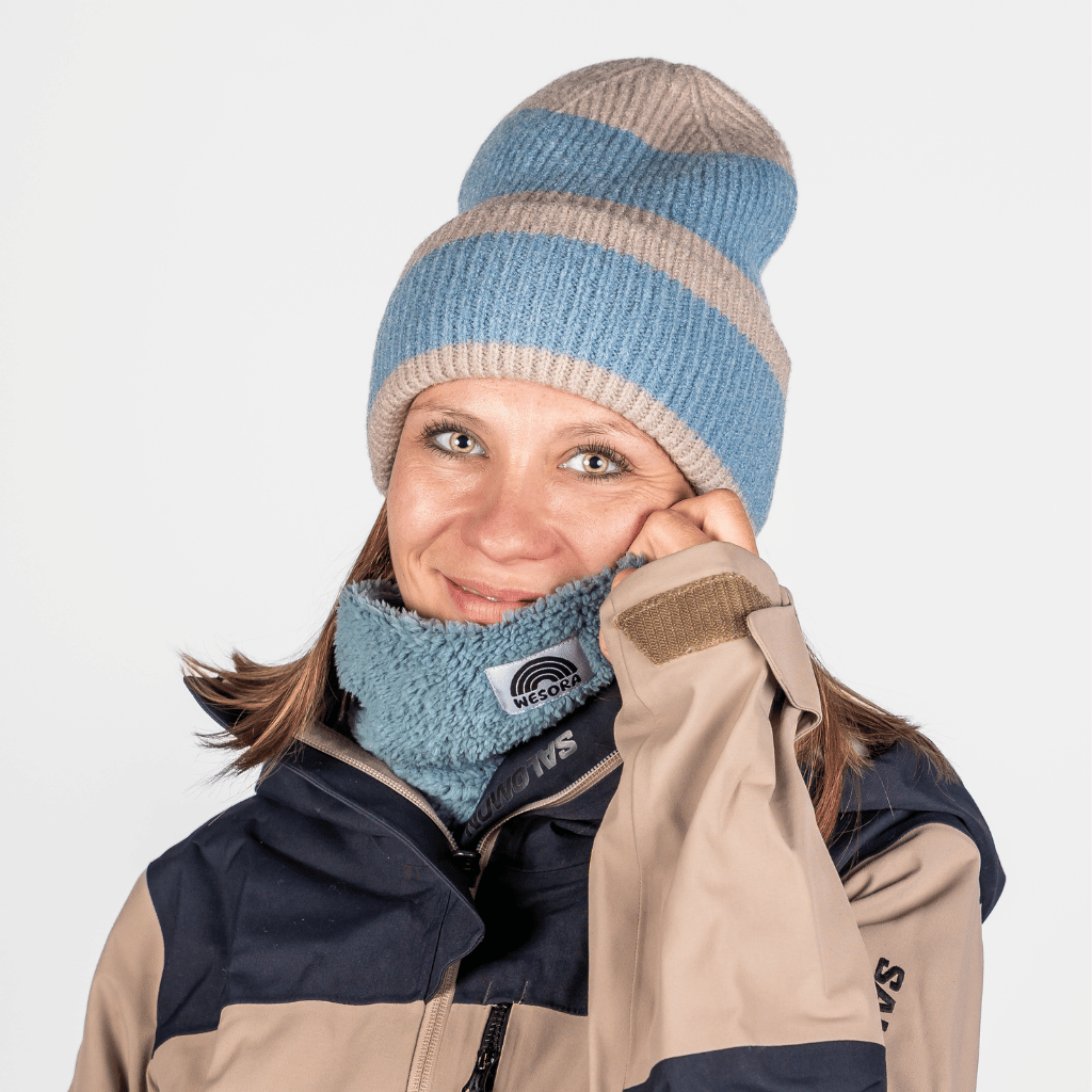 Neckwarmer & Beanie Bundle - Lagon, getragen von einer lächelnden Person in Winterkleidung, Hand an der „WESCORA“ Halswärmer, in einer kalten Umgebung.