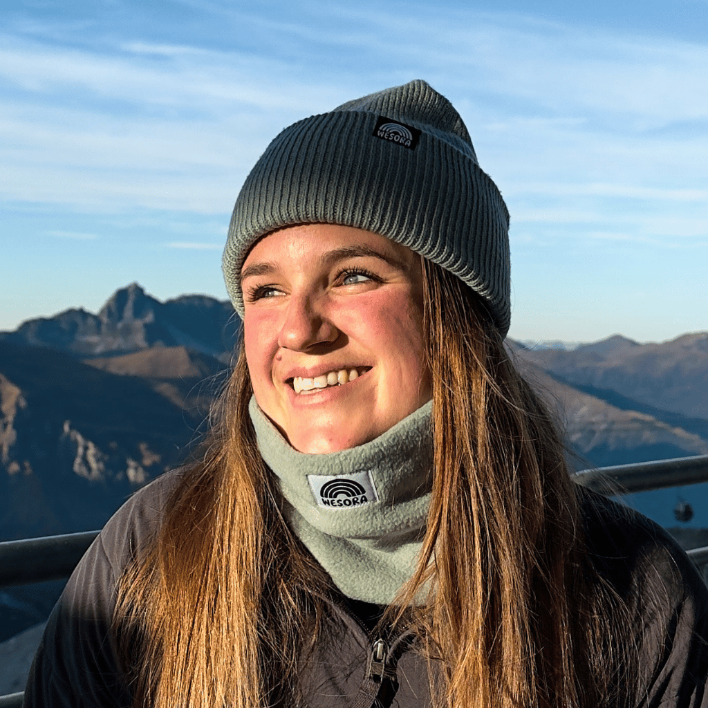 Neckwarmer & Beanie Bundle - Mint getragen von einer lächelnden Person im Winteroutfit, vor sonnenbeschienenen Bergen, seitlich blickend.