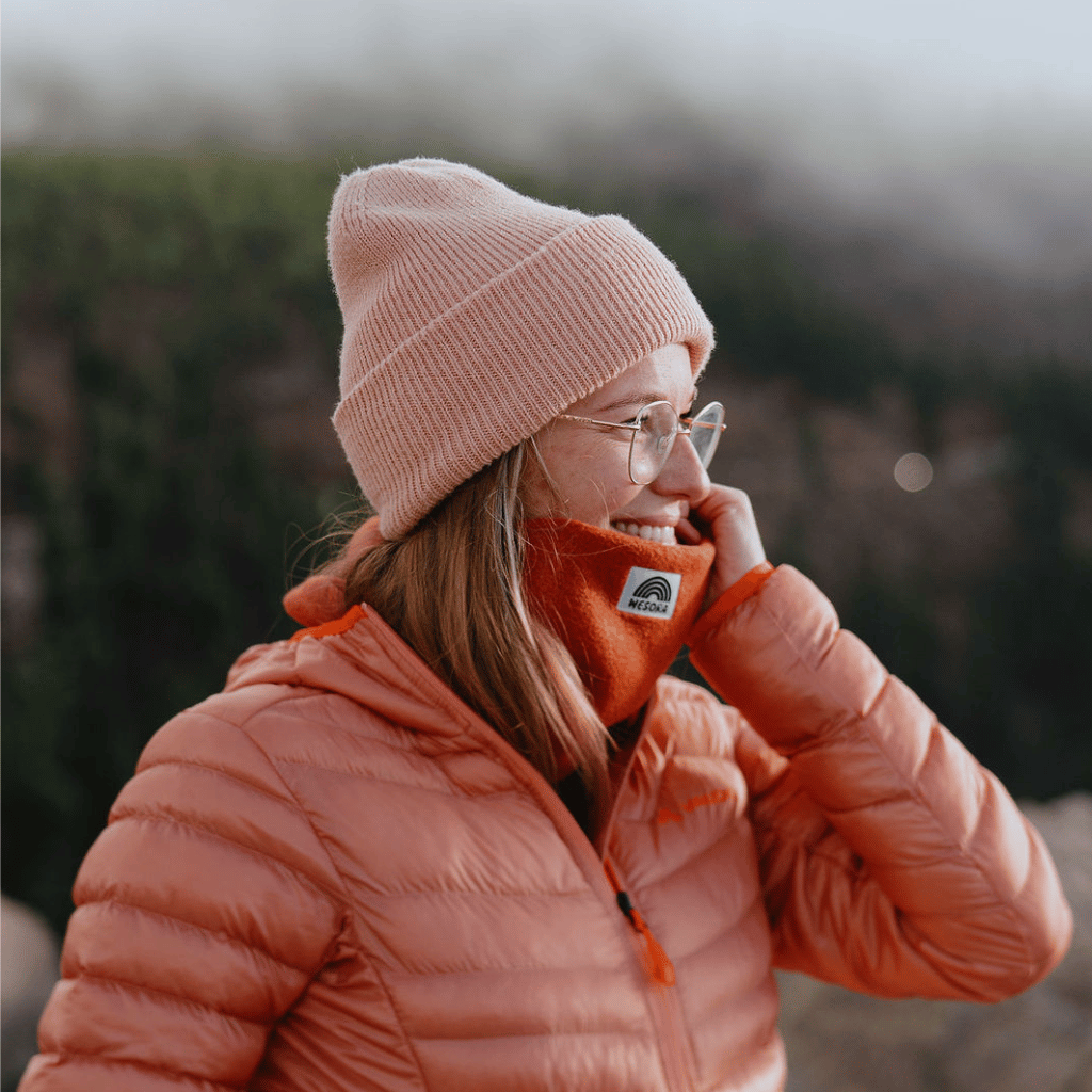 Neckwarmer & Beanie Bundle - Orange, getragen von einer Person in winterlicher Umgebung, lächelnd mit Hand am Gesicht, im Freien fotografiert.