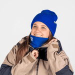 Neckwarmer & Beanie Bundle - Royal, getragen von junger Frau im Winteroutfit, die ihren Kragen anpasst, lächelnd vor winterlicher Kulisse.