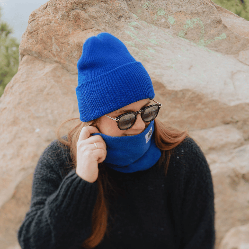 Neckwarmer & Beanie Bundle - Royal, getragen von einer Person vor einem Felsen, mit Sonnenbrille und schwarzem Pullover im Freien fotografiert.