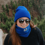 Neckwarmer & Beanie Bundle - Royal, getragen von lächelnder Person im Wald, von vorne fotografiert. Ideal für winterliche Outdoor-Abenteuer.