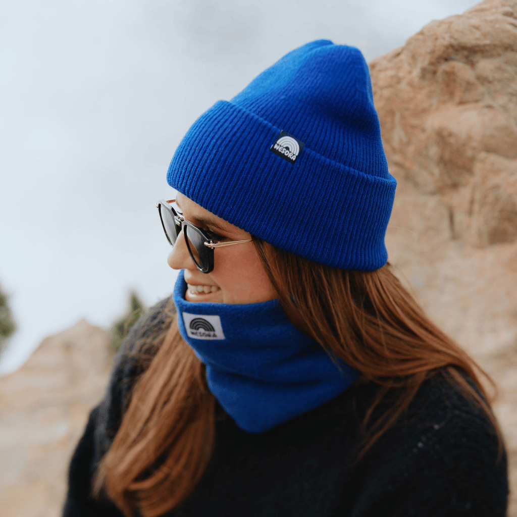 Neckwarmer & Beanie Bundle - Royal, getragen von einer Person im Profil mit Sonnenbrille, vor felsigem Hintergrund, vermittelt Wärme und Stil.
