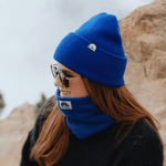Neckwarmer & Beanie Bundle - Royal, getragen von einer Person im Profil mit Sonnenbrille, vor felsigem Hintergrund, vermittelt Wärme und Stil.