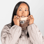 Pailetten Neckwarmer - Sparkle Gold mit roségoldenen Pailletten und weichem Fleece-Innenfutter, gehalten von Frau in beigem Steppmantel.