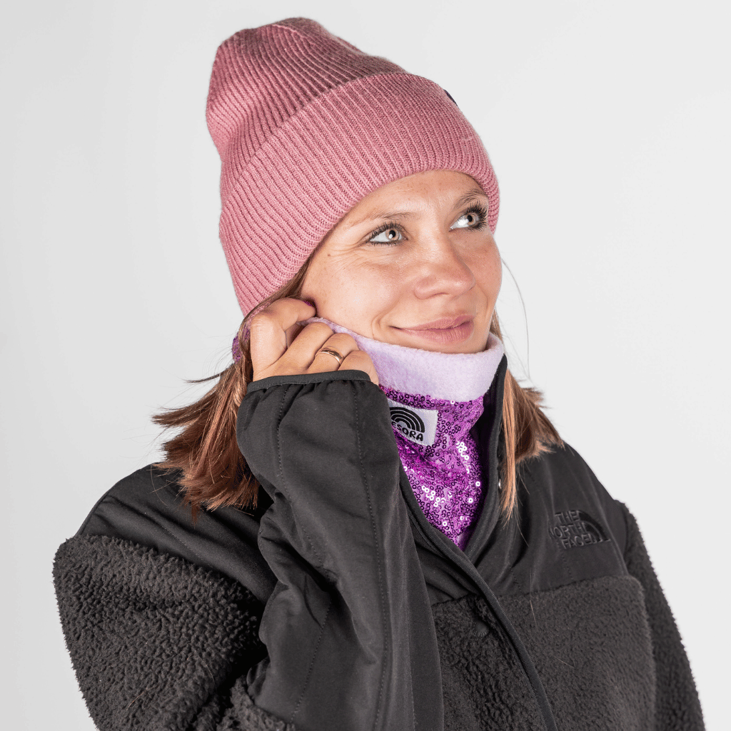 Pailetten Neckwarmer - Sparkle Lilac, getragen von einer Frau im Winterlook, die den glitzernden Flieder-Halswärmer über ihr Gesicht zieht.