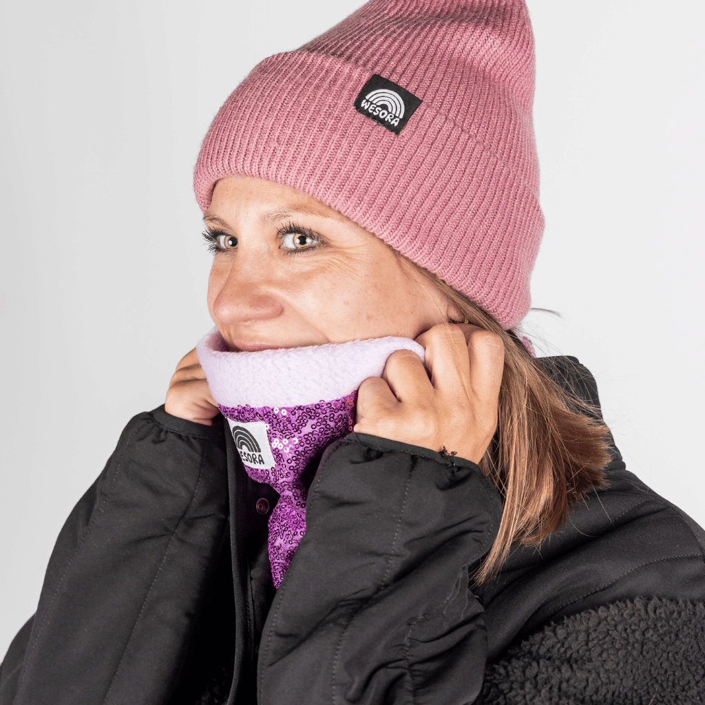 Pailetten Neckwarmer - Sparkle Lilac, getragen von einer Frau, die den Kragen ihres Mantels hält und leicht zur Seite schaut.