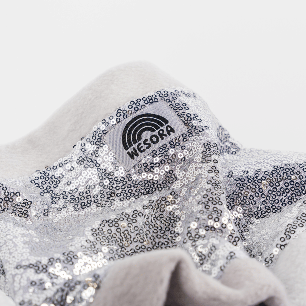 Pailetten Neckwarmer - Sparkle Silver mit silbernen Pailletten auf weißem Fleece, WESORA-Label sichtbar, Handarbeit aus Deutschland, designt in Österreich.