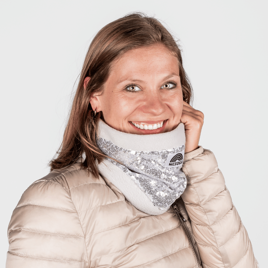 Pailetten Neckwarmer - Sparkle Silver mit schimmernden Details, getragen von einer lächelnden Frau in einem beigen Puffer-Jacke, frontal fotografiert.