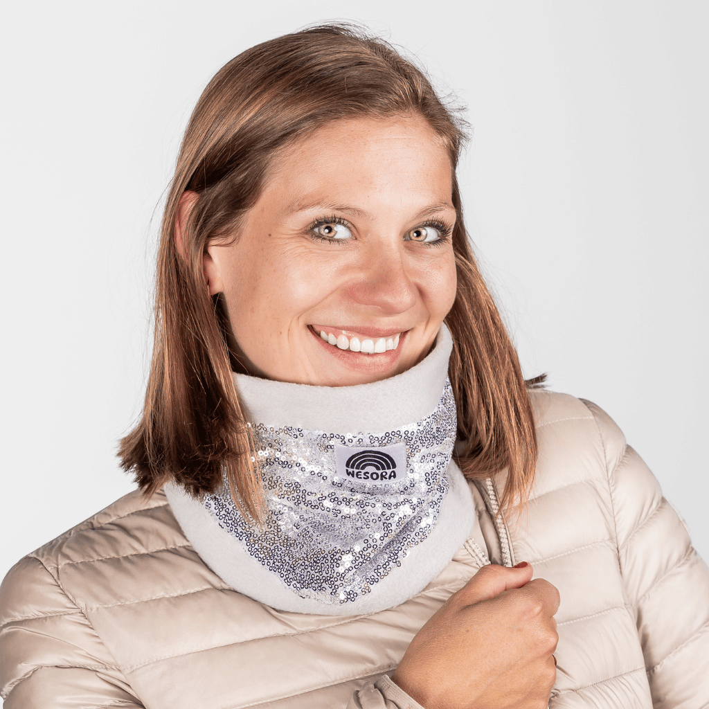 Pailetten Neckwarmer - Sparkle Silver mit schimmerndem Pailletten-Panel, getragen von lächelnder Frau in gesteppter Jacke, frontal aufgenommen.