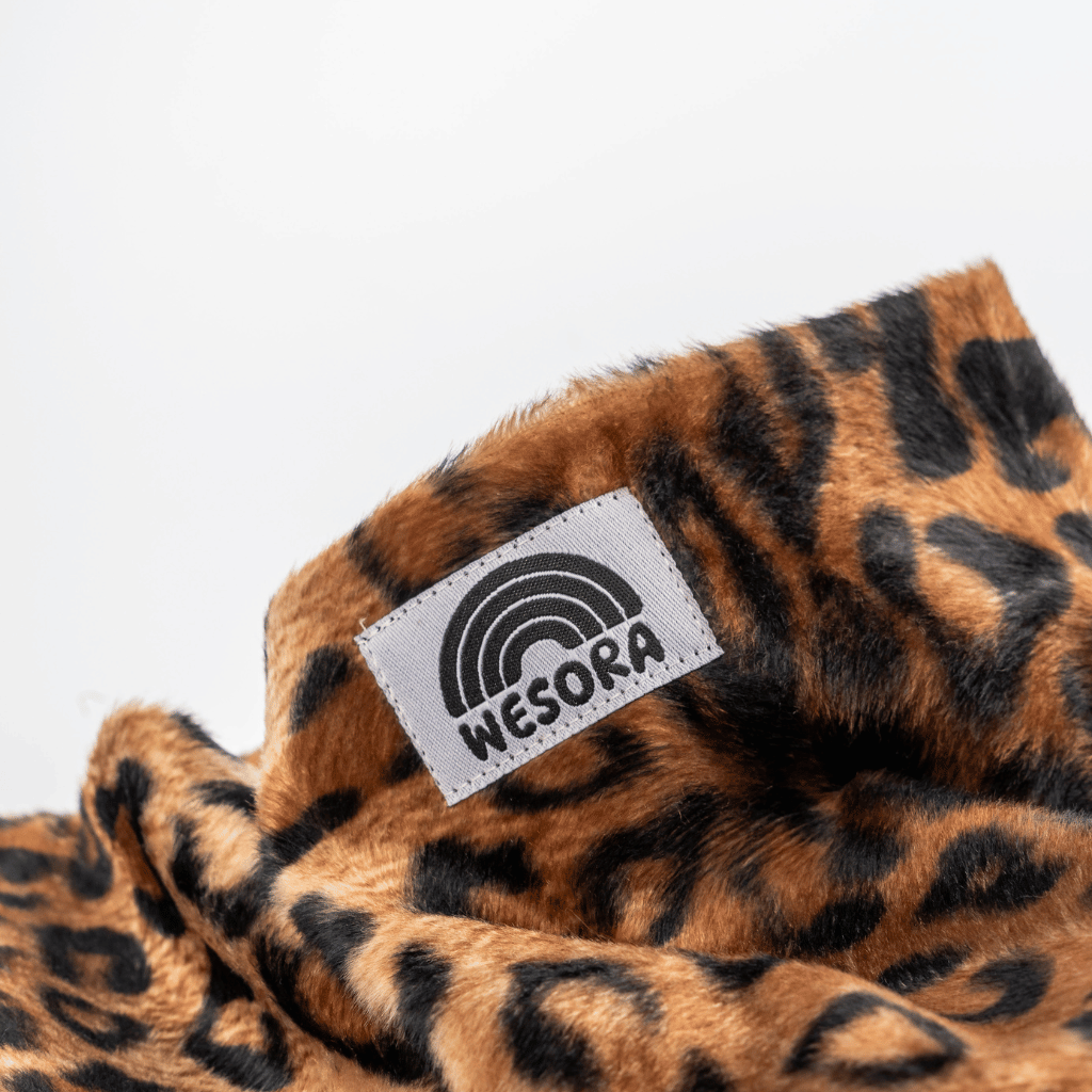 Printed Neckwarmer - Wild Leo Fur mit Leopardenmuster und WESORA-Label, fotografiert auf einer Nahaufnahme, betont wilde Eleganz und handgemachte Qualität.