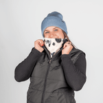 Printed Neckwarmer - Cow Spirit Fur mit Kuhmuster, getragen von Person in Winterkleidung, vor grauem Hintergrund, hält den Neckwarmer vor das Gesicht.