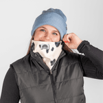 Printed Neckwarmer - Cow Spirit Fur mit Kuhmuster und WESORA-Logo, getragen von jungem Erwachsenen, der Gaiter zum Gesicht zieht, vor neutralem Hintergrund.