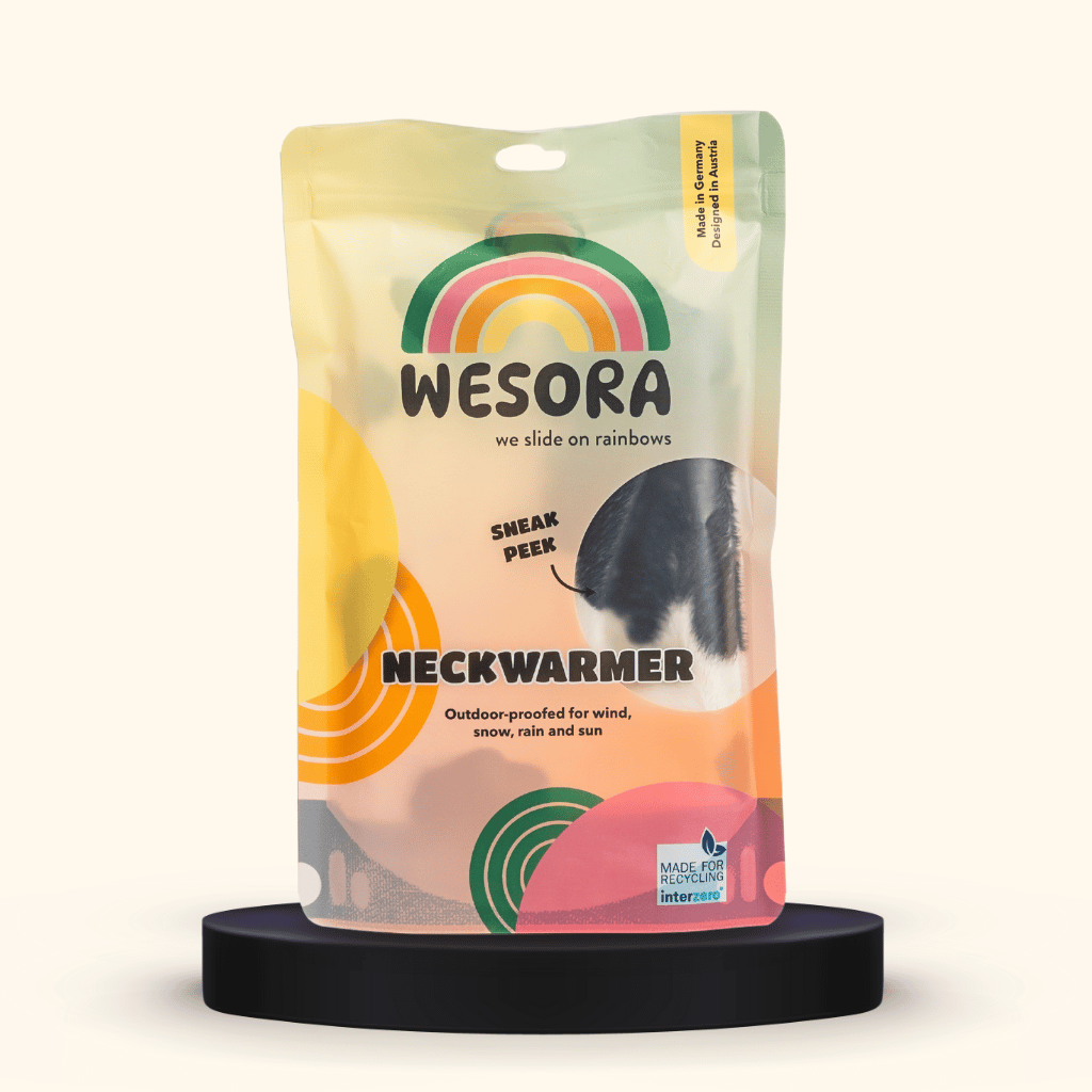 Printed Neckwarmer - Cow Spirit Fur mit modernem Kuhmuster, präsentiert auf einem schwarzen Podest, zeigt den recycelbaren Beutel mit Vorschaufenster.