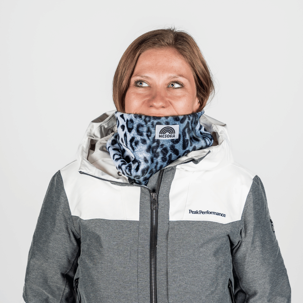 Printed Neckwarmer - Grey Leo Fur, in grauem Leopardenmuster, getragen von einer lächelnden Frau im Winteroutfit, fotografiert vor hellem Hintergrund.