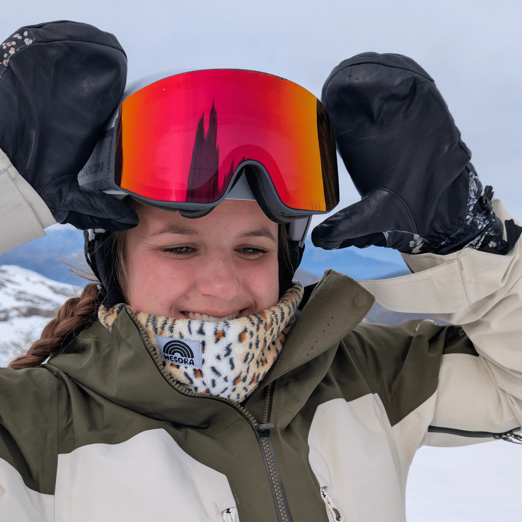 Printed Neckwarmer - Fluffy Wild Leo, getragen von einer Person beim Wintersport, fotografiert auf einer verschneiten Piste beim Anpassen der Skibrille.