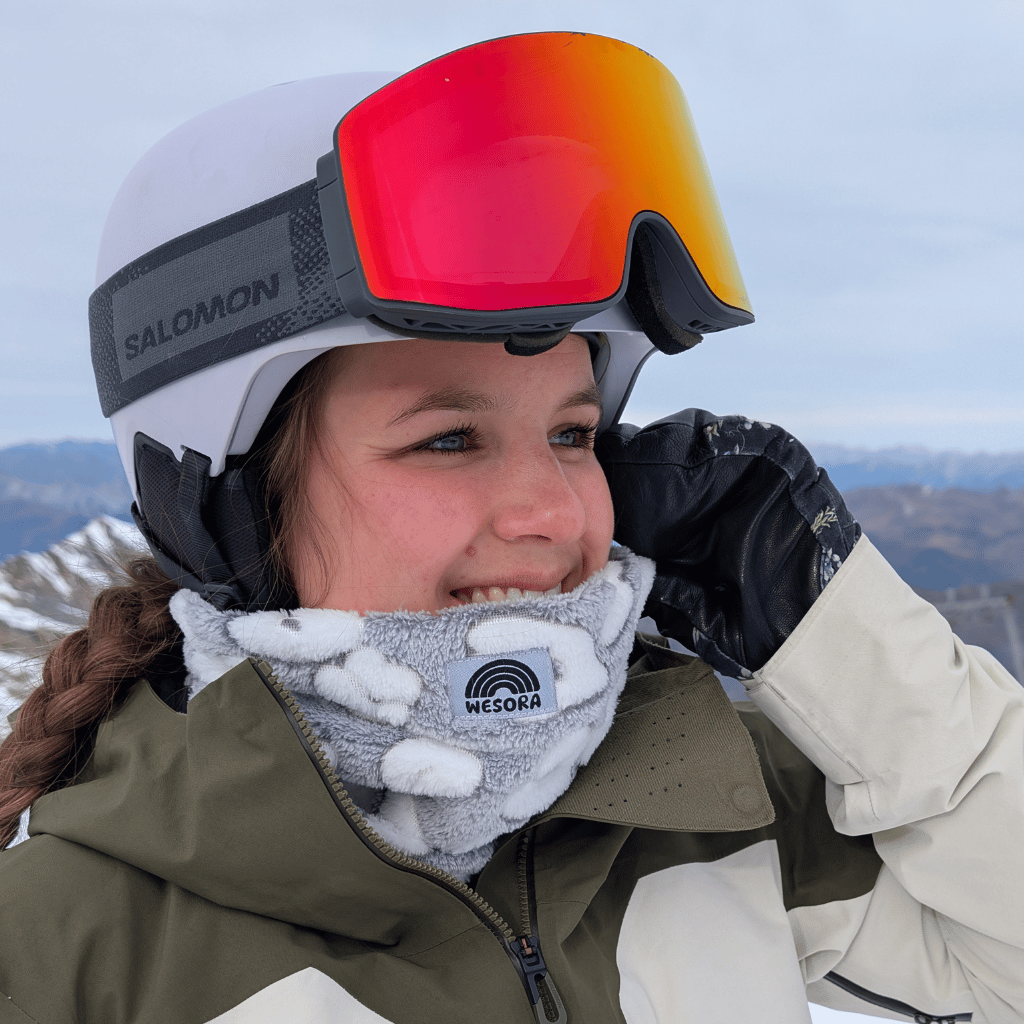 Printed Neckwarmer - Fluffy Grey Leo mit grau-weißem Leopardenmuster, getragen von Wintersportler vor schneebedeckten Gipfeln, lächelnd zur Seite blickend.