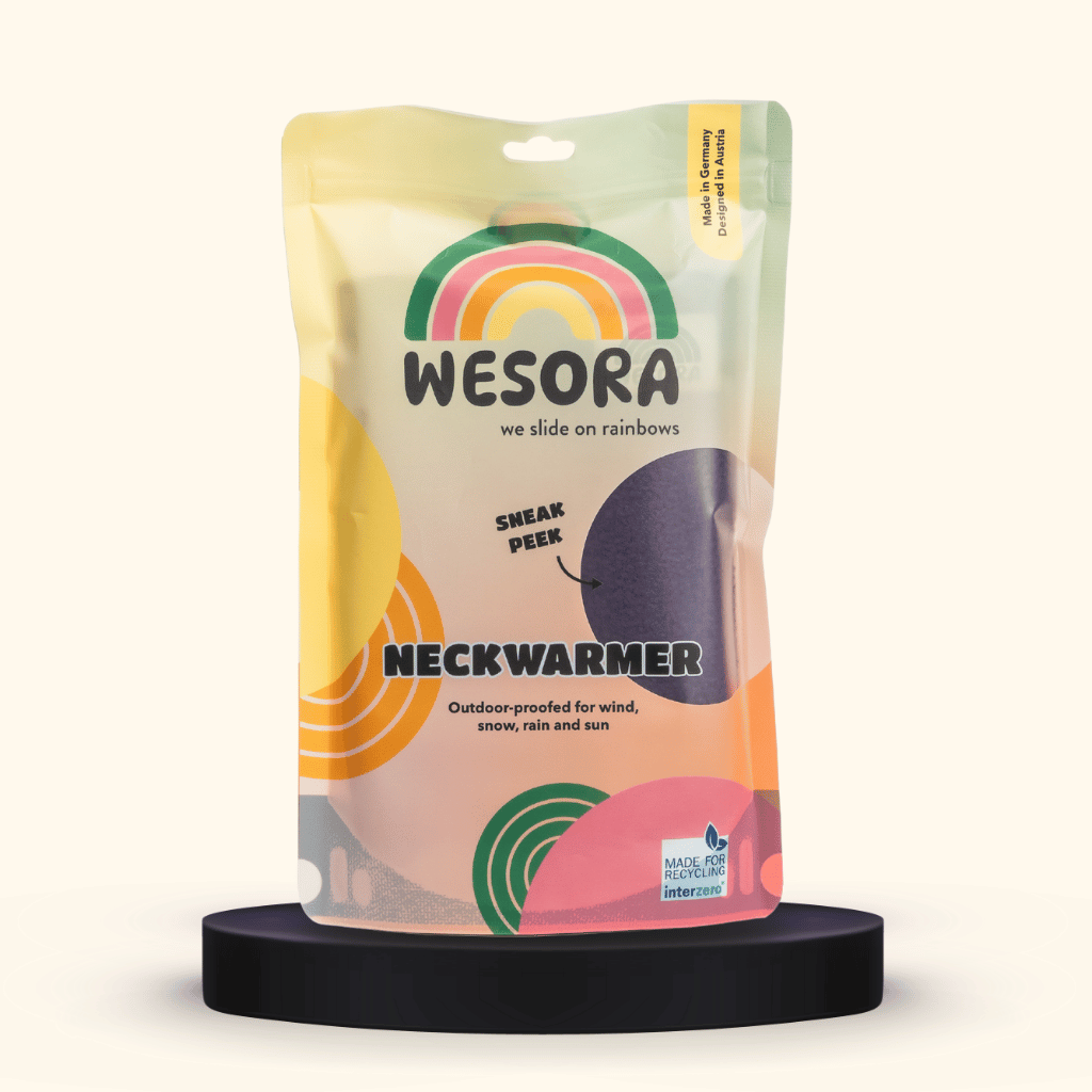 Fleece Neckwarmer - Purple Noir im pastellfarbenen Standbeutel mit Regenbogen-Design, durchsichtigem Fenster, auf schwarzem Sockel, Outdoor-proofed und recycelbar.