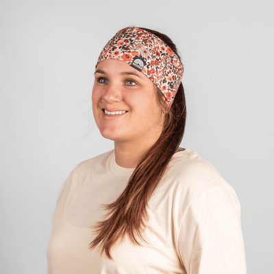 Stirnband - Red Blossom mit floralen Mustern, getragen von junger Frau mit braunen Haaren in einem neutralen Hintergrund, seitlich lächelnd fotografiert.