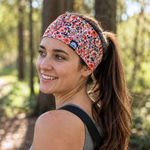 Stirnband - Red Blossom mit floralem Muster, getragen von einer jungen Frau im Wald, seitlich lächelnd, mit Sonnenlicht im Hintergrund.