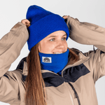 Fleece Neckwarmer - Royal Blue, getragen von einer lächelnden Person, die den blauen Beanie anpasst. Ideal für stilvolle, verantwortungsvolle Outdoor-Abenteuer.