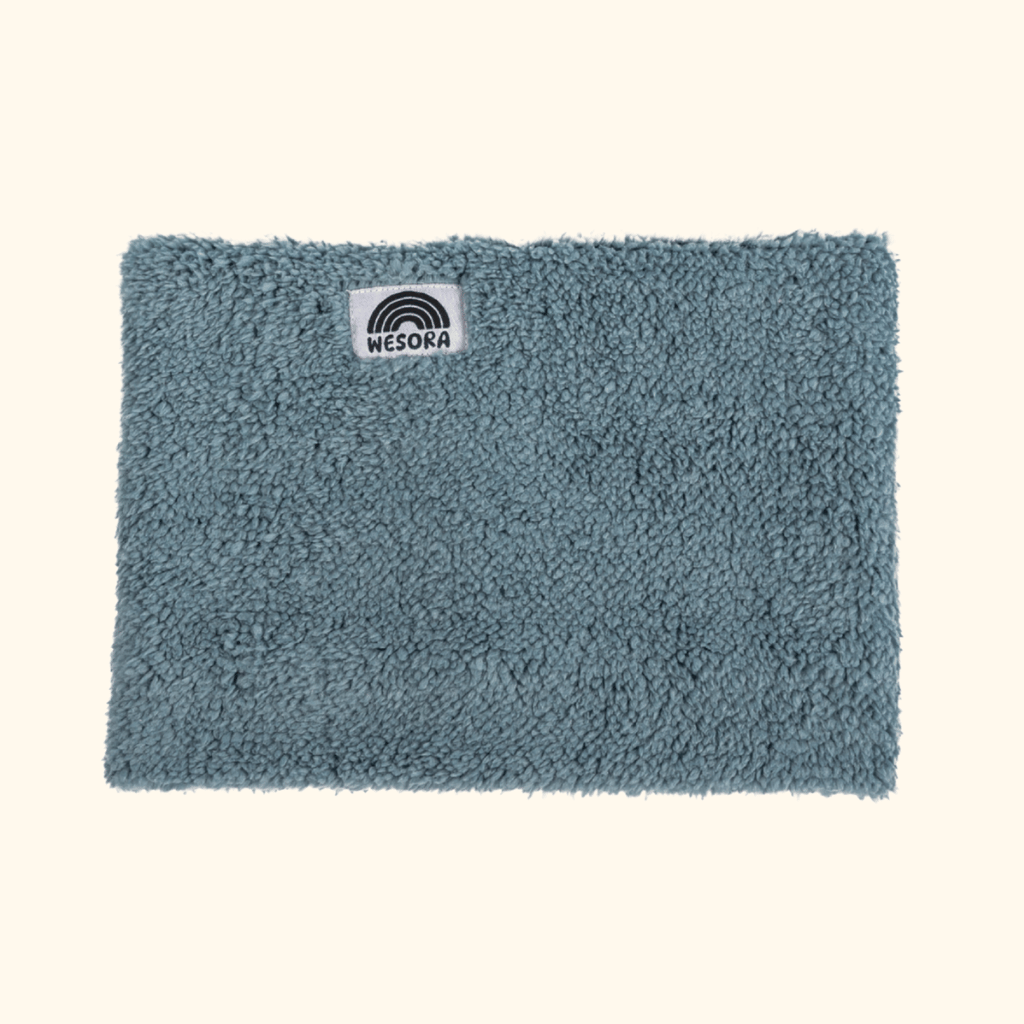 Sherpa Neckwarmer - Fluffy Blue mit weißem Label, fotografiert flach liegend, zeigt stilisiertes Regenbogenmotiv und Markennamen WESORA.