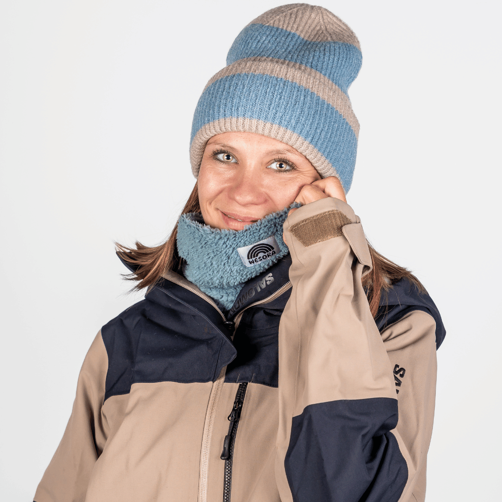 Sherpa Neckwarmer - Fluffy Blue, getragen von einer Frau in Winterjacke, zeigt sanftes Lächeln und hält den flauschigen Halswärmer nah ans Gesicht.