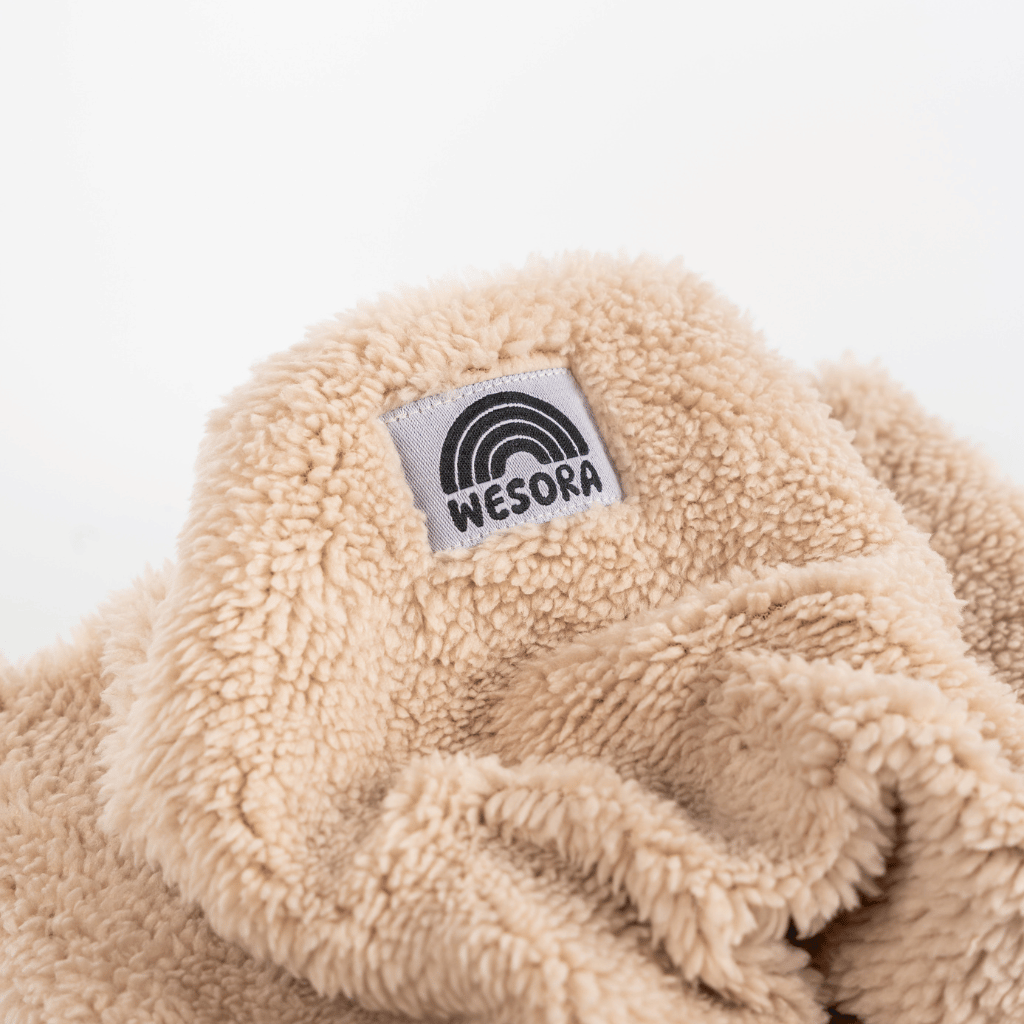 Sherpa Neckwarmer - Fluffy Beige mit WESORA-Label und Regenbogenlogo, nah gezeigt, aus weichem, beigem Fleece, handgefertigt in Deutschland.