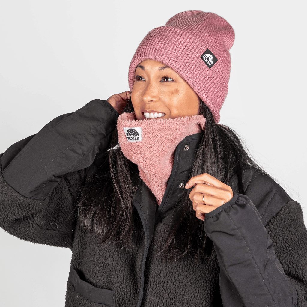 Sherpa Neckwarmer - Fluffy Rose, getragen von einer lächelnden Person, die das rosa Accessoire anpasst, fotografiert in einem Studio.