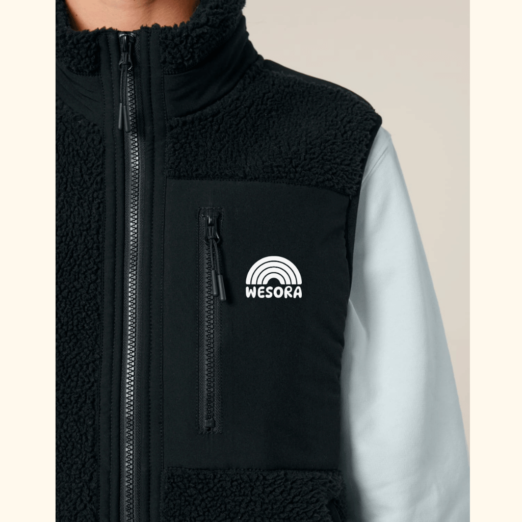 Sherpa Weste - Unisex mit Reißverschluss und Brusttasche, getragen über einem langärmeligen Shirt, zeigt das WESORA-Logo mit Regenbogenmotiv.