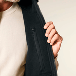 Sherpa Weste - Unisex mit Reißverschluss, offenbart eine Innentasche. Darunter ein Crewneck-Shirt erkennbar, getragen in einer Nahaufnahme.