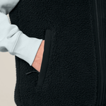 Sherpa Weste - Unisex mit Reißverschlusstasche, getragen über einem langärmeligen Oberteil, Hand in der Tasche, Nahaufnahme.