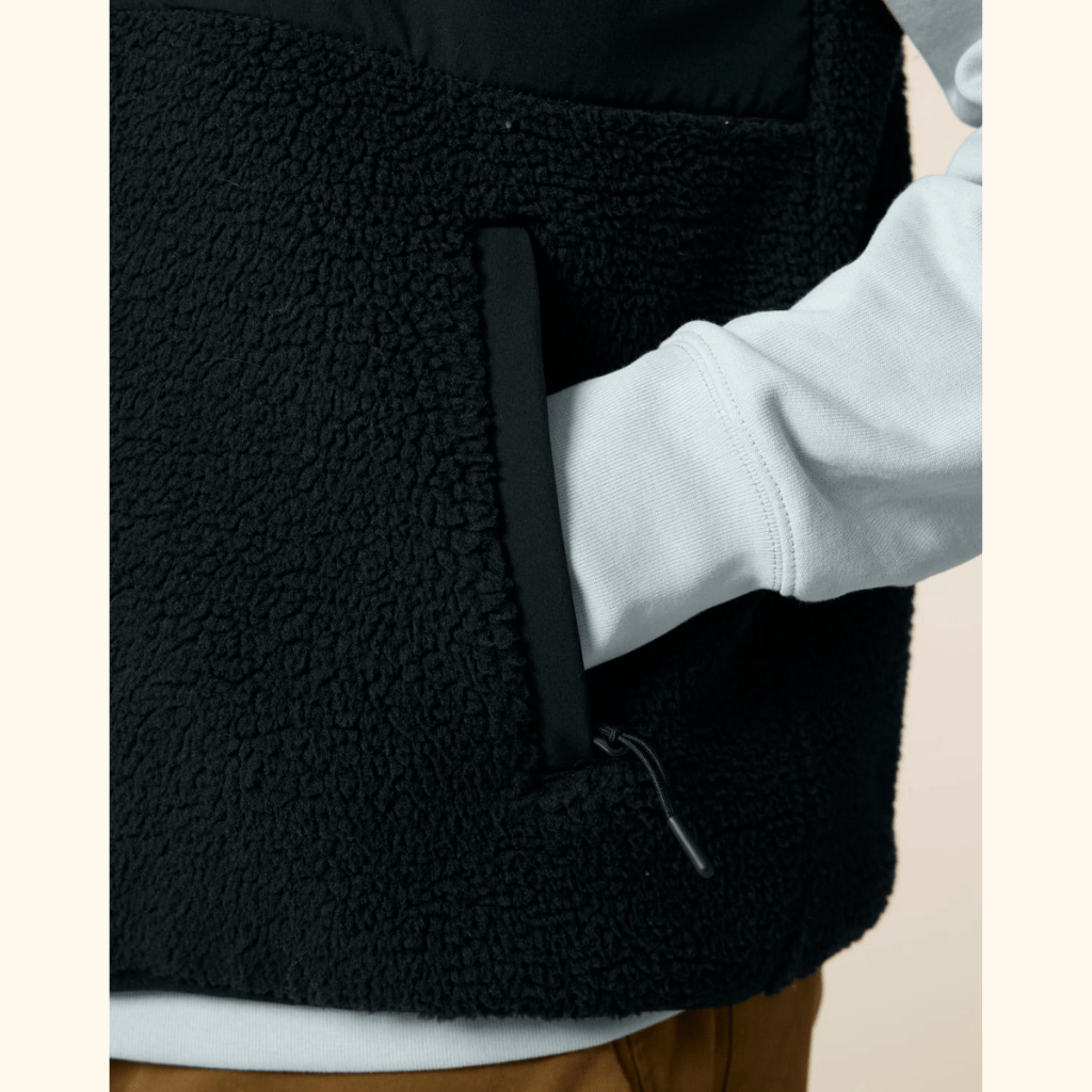 Sherpa Weste - Unisex mit sichtbarer, texturierter Fleece-Oberfläche, Hand in der Fronttasche mit Kordelzug, über einem hellen Langarmshirt getragen.