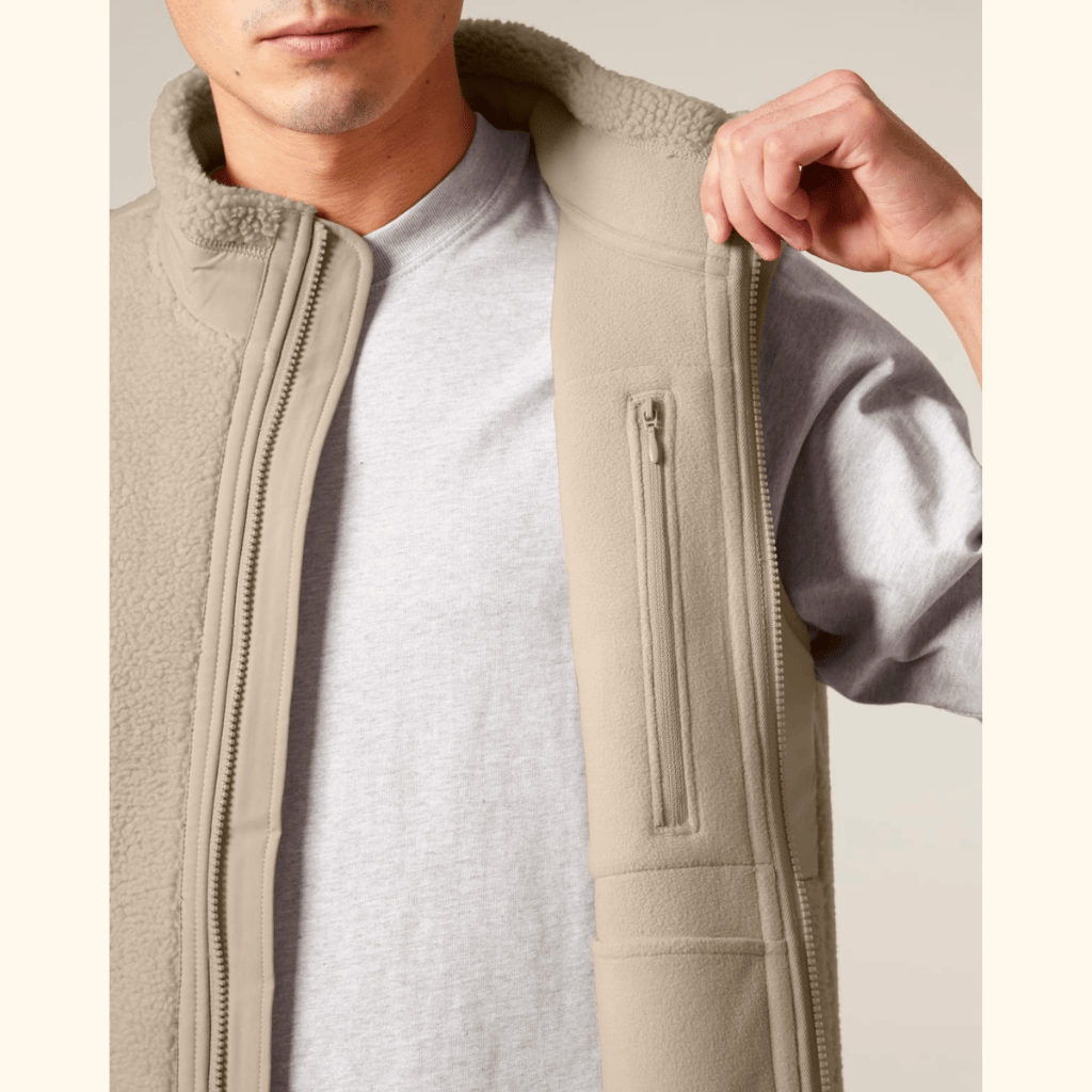 Sherpa Weste - Unisex mit Reißverschlusstasche innen, getragen über einem grauen T-Shirt, von Person an einer Seite geöffnet gezeigt.