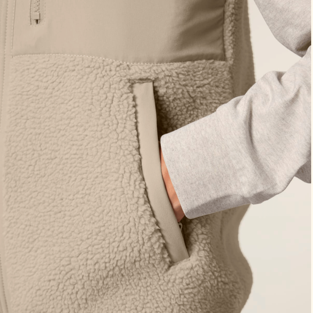 Sherpa Weste - Unisex mit seitlicher Tasche, getragen von einer Person in grauem Langarmshirt, fotografiert in Nahaufnahme mit Hand in der Tasche.