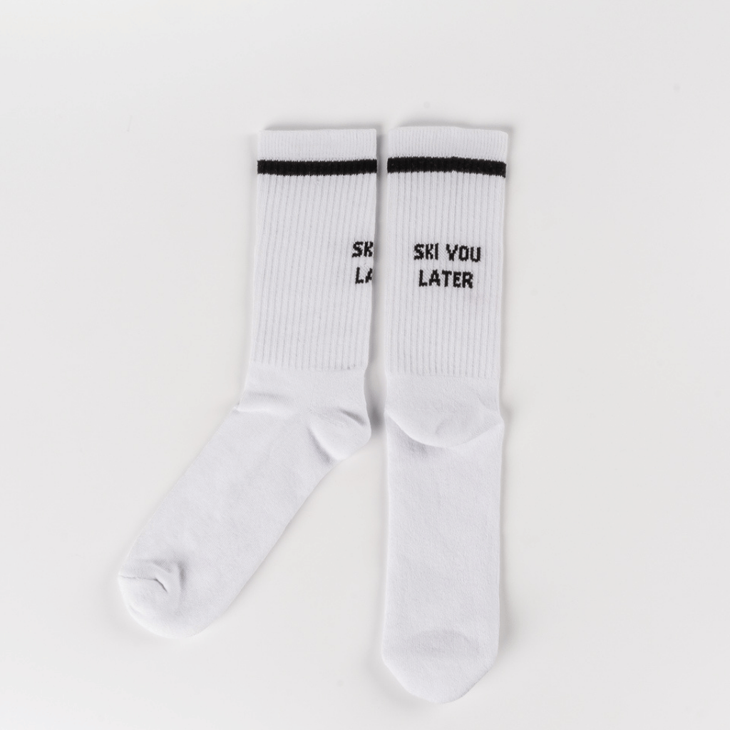 Socks - Ski you later mit schwarzem Streifen und Slogan SKI YOU LATER auf weißem, geripptem Stoff, flach ausgelegt.