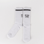 Socks - Ski you later mit schwarzem Streifen und Slogan SKI YOU LATER auf weißem, geripptem Stoff, flach ausgelegt.