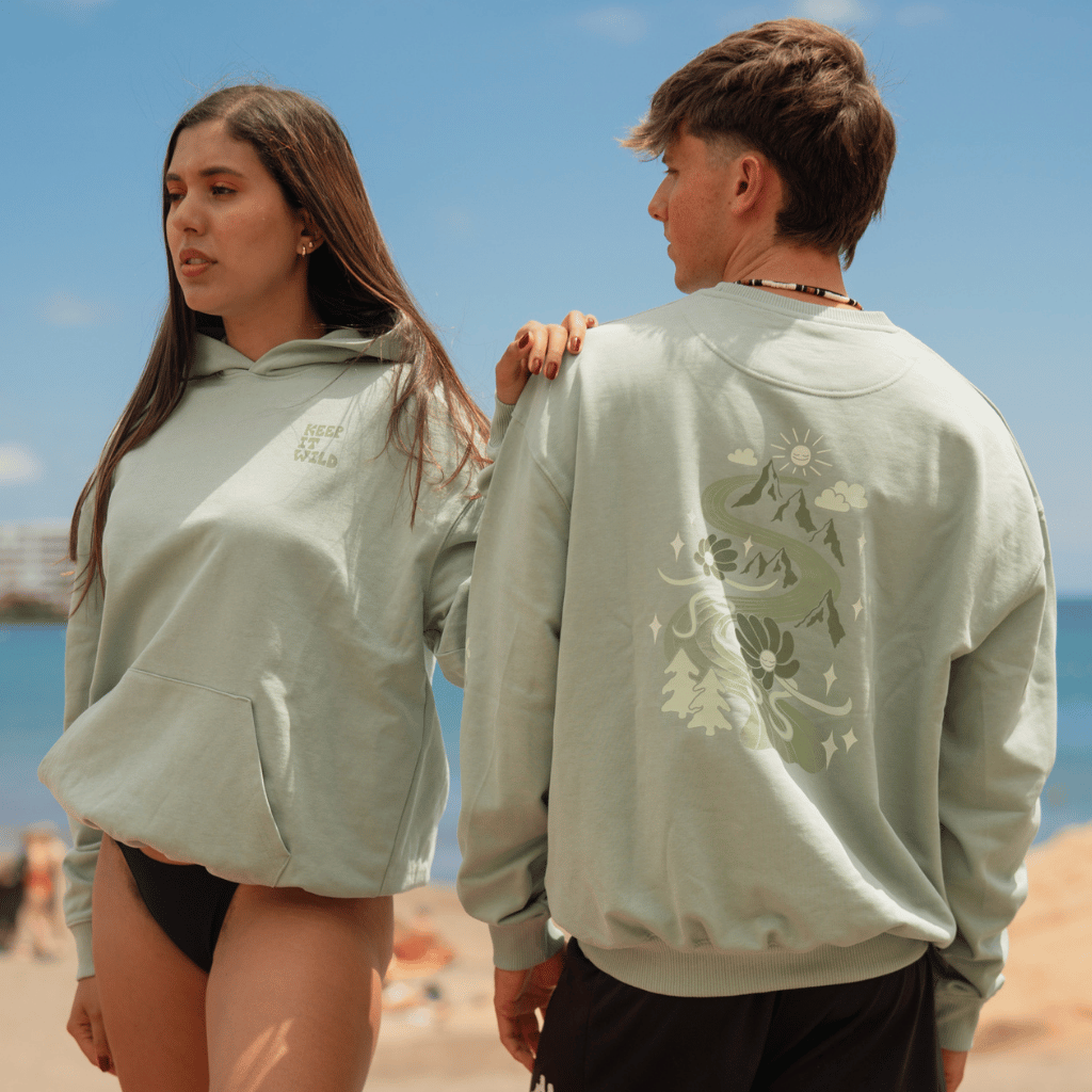 We Slide on Rainbows - Unisex Sweatshirt mit verspieltem Design, getragen von Mann und Frau, fotografiert am Strand, Frau frontal posiniert zur Kamera, Mann mit Rücken, so das Vorder- und Rückendruck erkenntlich ist.