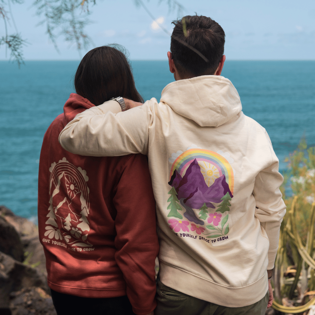Space to Grow Mountain - Unisex Pullover mit Bergmotiv und Give Yourself Space to Grow-Text, getragen von zwei Personen am Meer, von hinten fotografiert.