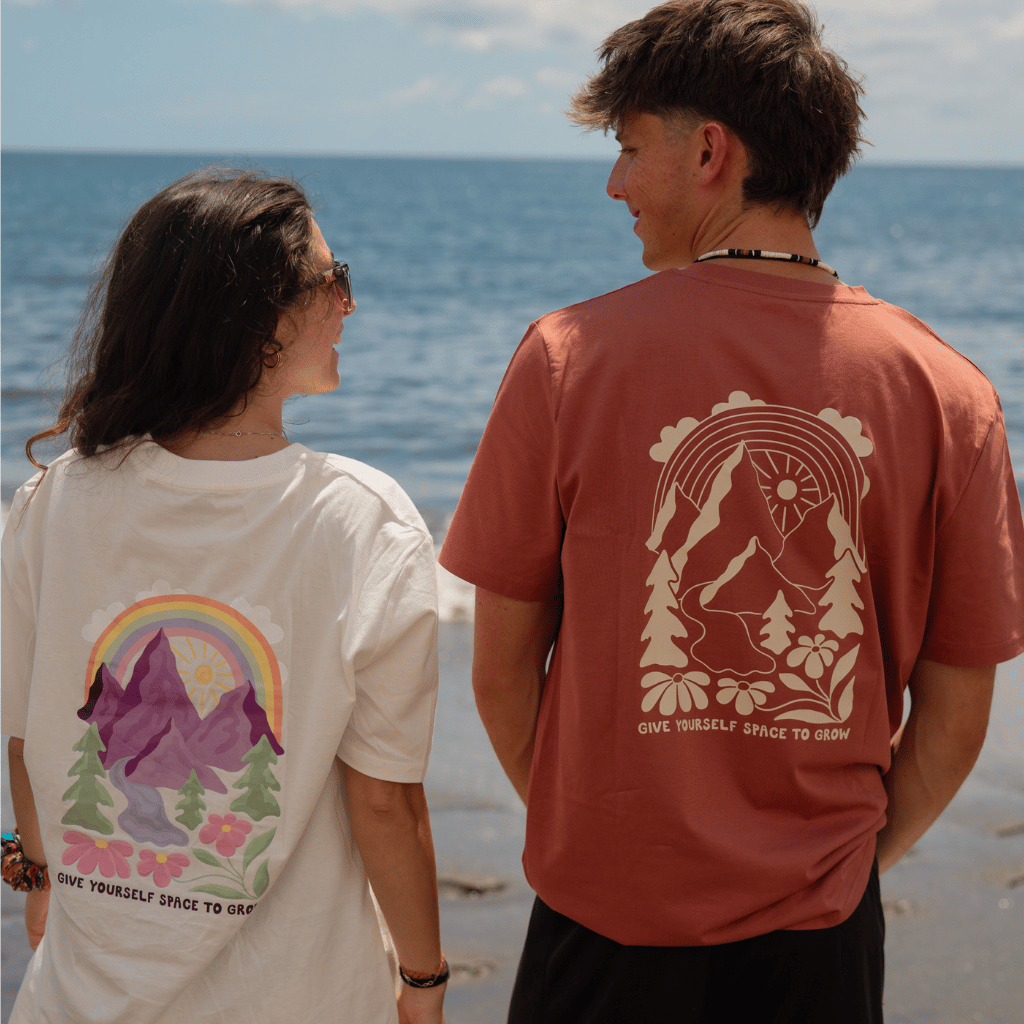 Space to Grow Mountain - Unisex Tshirt mit Berg-, Baum-, Blumen- und Regenbogenmotiven, getragen von zwei Personen am Strand, Rückenansicht.