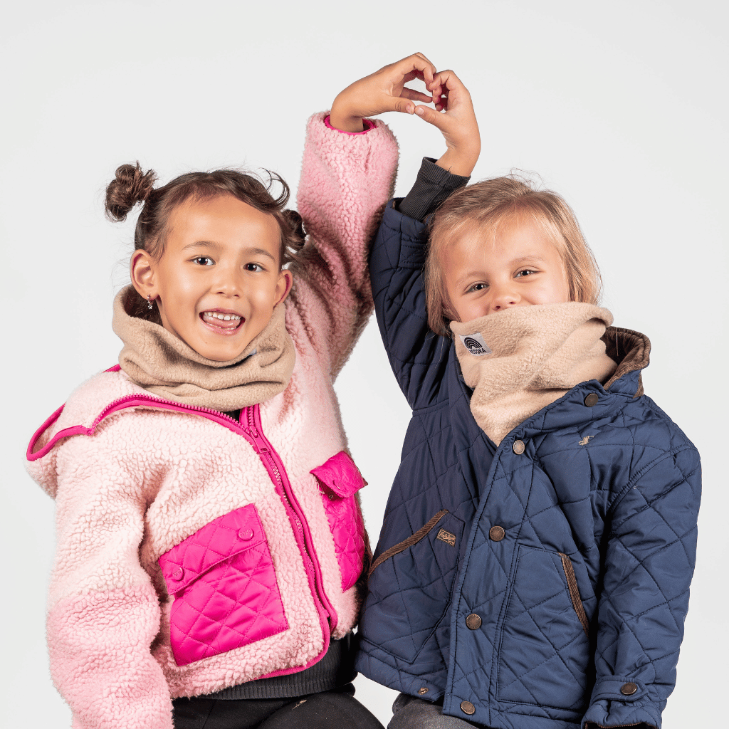 Fleece Neckwarmer - The Teddy Kid, getragen von zwei fröhlichen Kindern in Winterjacken, fotografiert vor einem neutralen Hintergrund, beide mit erhobenen Armen.