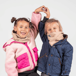 Fleece Neckwarmer - The Teddy Kid, getragen von zwei fröhlichen Kindern in Winterjacken, fotografiert vor einem neutralen Hintergrund, beide mit erhobenen Armen.