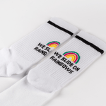 Socken - WESORA mit Regenbogenmotiv und WE SLIDE ON RAINBOWS-Schriftzug, flach ausgebreitet, sportlicher Stil, schwarze Streifen unter dem Bund.