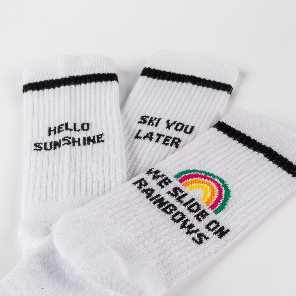 WESORA Socken-Bundle: Drei weiße Crew-Socken mit schwarzen Slogans und Regenbogenmotiv, auf weißem Hintergrund ausgelegt.