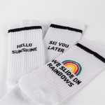 WESORA Socken-Bundle: Drei weiße Crew-Socken mit schwarzen Slogans und Regenbogenmotiv, auf weißem Hintergrund ausgelegt.
